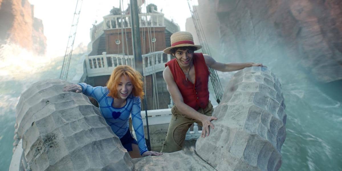 Luffy and Nami holding onto rocks amid waves, smiling